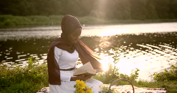Black Woman in White Dress Reading at the River Bank