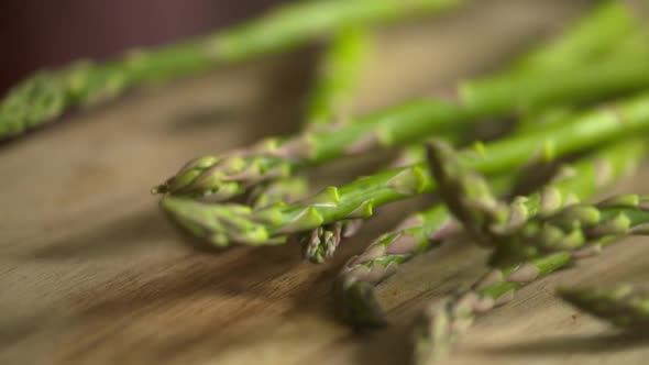 Slow motion footage of a bunch of fresh, green asparagus falling on to a wood cutting board