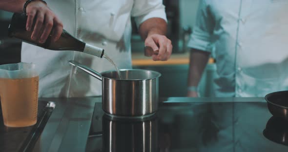 Chef pours bottle of wine into pot as other looks on