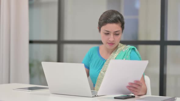 Indian Woman with Laptop Reading Documents in Office