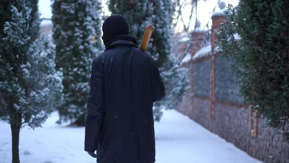 Back View Burglar with Baseball Bat Walking on Snowy Backyard Outdoors