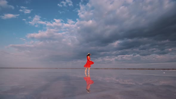Woman Tourist in a Waving Dress Walks Along a Salt Lake in Which the Sky Is Reflected