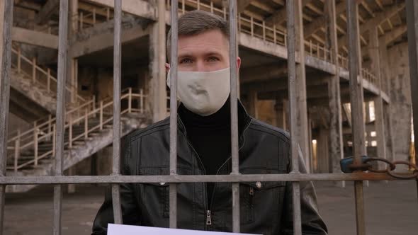 Portrait of a Man in a Medical Mask with the Inscription Covid-19 Behind a Fence