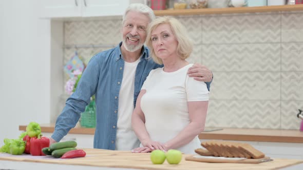 Loving Old Couple Looking at Camera in Kitchen