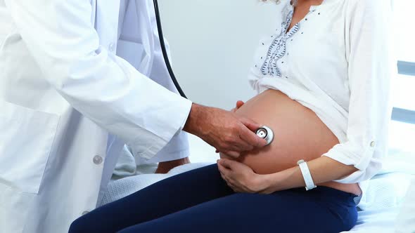 Doctor examining pregnant womans belly with stethoscope in ward