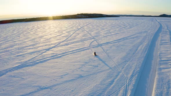 Aerial view single snowmobile driver travelling fast across vast snowy Nordic winter wilderness away