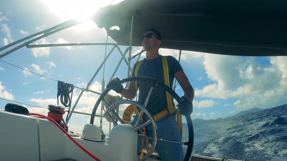 A Man in Sunglasses is Handling a Wheel of a Sailboat