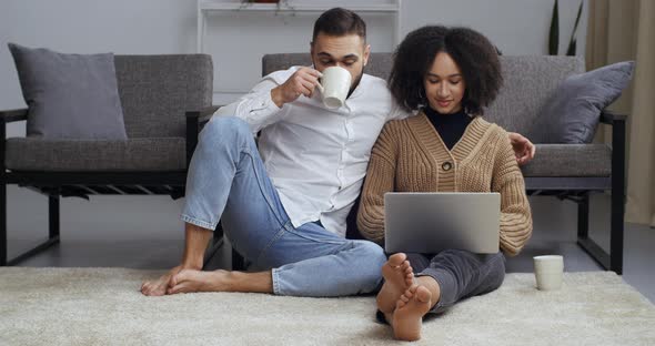 Interracial Couple Looks at Laptop Screen of Modern Computer Wife Husband Use Technologies for