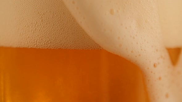 Detail of Pouring Fresh Beer with Foam Running Down Golden Background