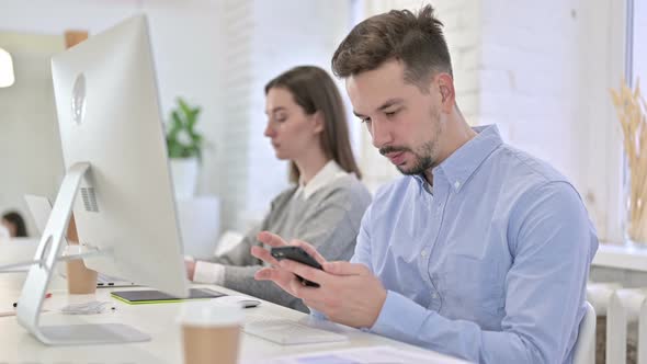 Serious Creative Professional Using Smartphone in Office