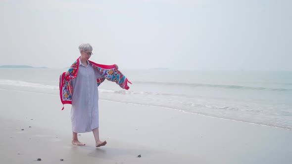 Asian retired woman relaxing by the sea in summer. A senior woman walking on the beach.