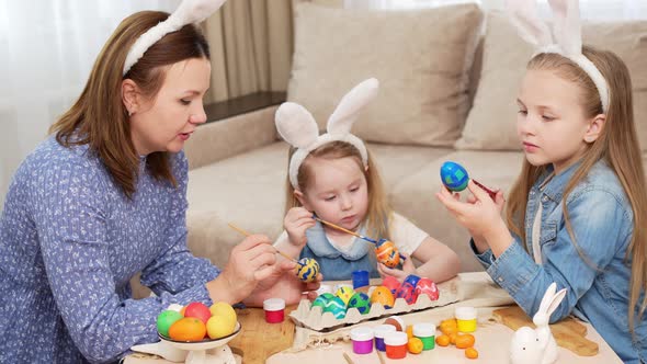 Mom and Daughters with Rabbit Ears Decorate Easter Eggs with Paints
