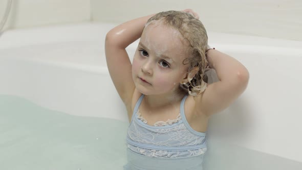 Cute Blonde Girl Takes a Bath in Swimwear. Little Child Washes Her Head