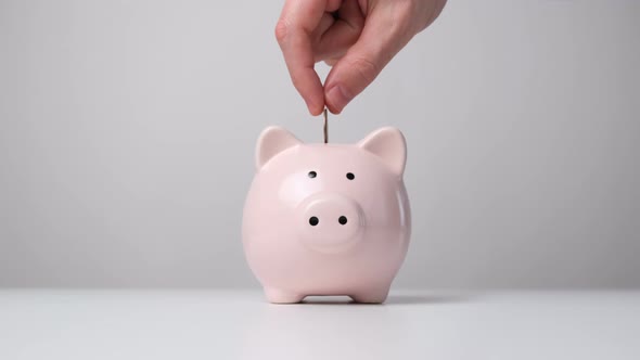 Hand Putting Coin Into Piggy Bank Front View