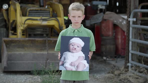 Slow motion of boy showing photo of himself as baby with cleft palate.