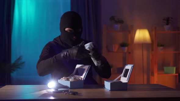 Thief in a Balaclava Finds Jewelry and Money on a Table in the House