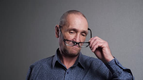 Senior Man Takes Off Glasses Rubbing Eyes on Grey Background