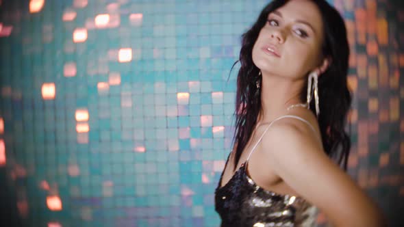 Portrait of a Sexy Brunette Woman with Earrings and a Silver Top on Shiny Background in the Studio