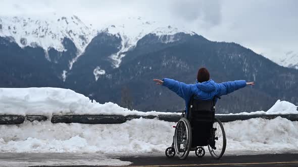 A Woman in a Wheelchair Raises Her Arms to the Sides and Thinks She is Flying in the Snowy Mountains