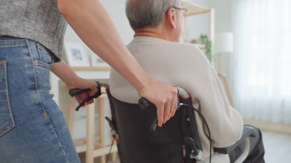 Asian young daughter take care senior male while sitting on wheelchair in living room at home