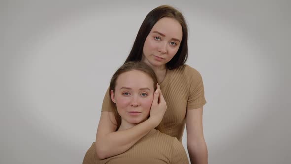 Front View Young Woman Touching Face of Twin Sister Posing at Grey Background