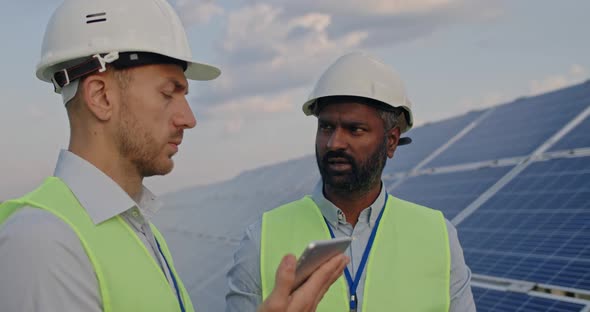 Close Up of Male Engineers Checking Work of Solar Panels and Communicating. Men in Hard Helmet and