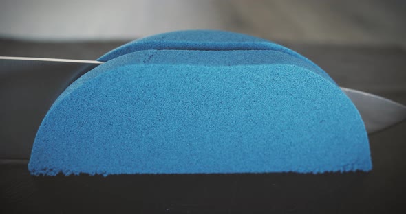 Blue kinetic sand is cut with a large knife. Relaxation techniques. Close-up.