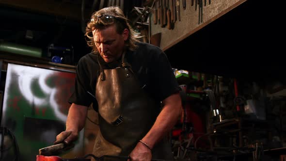 Blacksmith using wire brush on hot iron