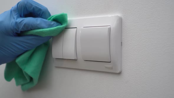 A Cleaner Man Wearing Gloves and a Mask Disinfects Electrical Light Switches  to Prevent COVID 19