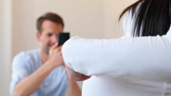 Man photographing pregnant womans belly at home 