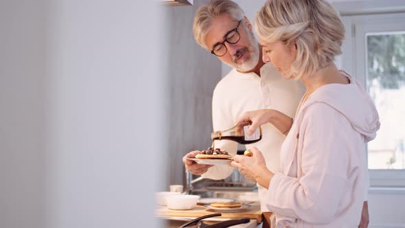 Mature woman pouring sirup over pancakes