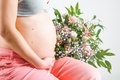 Pregnant woman with bouquet of flowers. Girl in gray top, pink pants holds hands on naked belly.  - PhotoDune Item for Sale