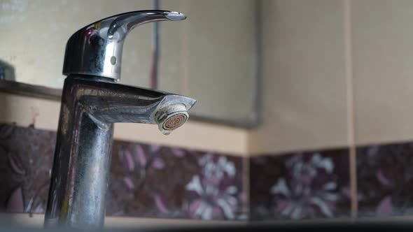 Close-up of a dirty faucet from which water is dripping