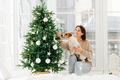 Happy housewife with broad smile, poses near decorated firtree with dog who smells bauble - PhotoDune Item for Sale