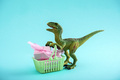 Funny green dinosaur toy with shopping basket full of present boxes on a blue background.  - PhotoDune Item for Sale