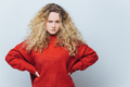 displeased angry woman with curly hair, keeps hands on waist, wears loose sweater - PhotoDune Item for Sale