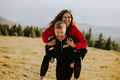 Young woman riding piggyback on a boyfriend at green hills - PhotoDune Item for Sale