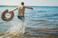 adult man running into water with splashes holding rubber inflatable ring. Back to childhood - PhotoDune Item for Sale