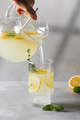 Lemonade with fresh lemon slices is poured from a jug into a glass. Summer drink with lemon. - PhotoDune Item for Sale