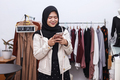 Young Muslim woman working at clothing shop while using phone receiving online orders. - PhotoDune Item for Sale