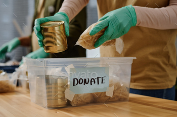 Close-up of gloved hands of volunteer putting food products into plastic box
