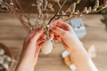 Close-up of a girl's hands hanging a decorative Easter egg on a willow branch at home.  - PhotoDune Item for Sale