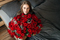 A beautiful girl is sitting on a bed in the bedroom with a huge bouquet of scarlet roses.  - PhotoDune Item for Sale