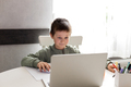 A schoolboy boy sits at a table in front of a laptop and studies dma. Distance learning for children - PhotoDune Item for Sale