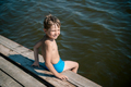 cute caucasian boy sitting on wooden pier diving into lake in countryside - PhotoDune Item for Sale