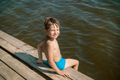 cute caucasian boy sitting on wooden pier diving into lake in countryside - PhotoDune Item for Sale