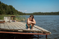 cute caucasian boy sitting on wooden pier sad and cold after swimming in lake - PhotoDune Item for Sale