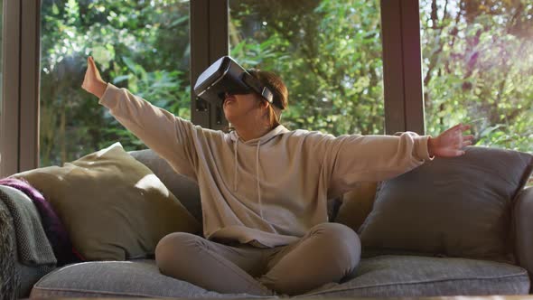 Asian girl smiling and gesturing while wearing vr headset sitting on the couch at home