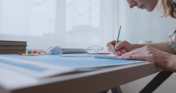 A young woman works and studies architecture from blueprints. She draws with a pencil in a notebook