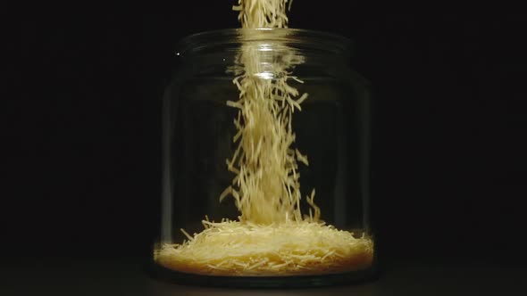 SLOW MOTION: Uncooked Filini Pasta Falls Into Empty Glass Jar On Black Background - Front View